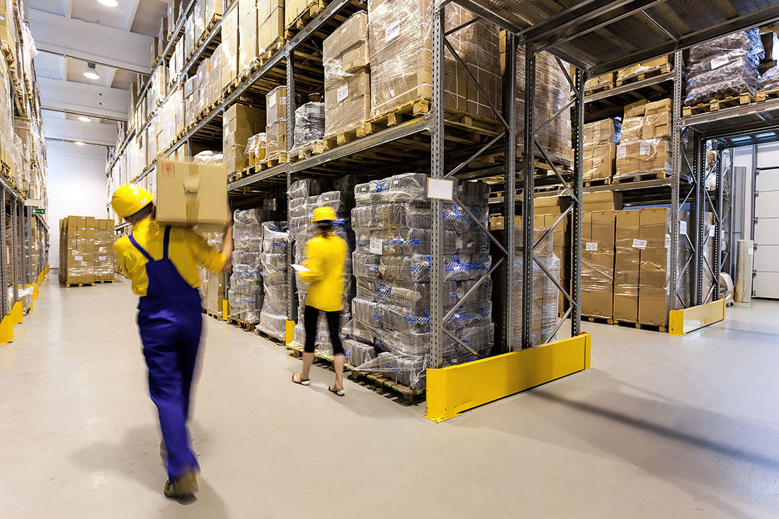 Warehouse worker carrying a box and a manager controlling products on the floor